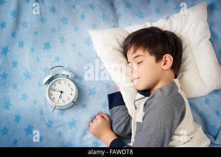 Sei anni bambino che dorme nel letto con la sveglia Foto Stock