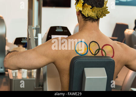 Ragazzo muscolare con Golden corona di alloro sulla testa e Olympic emblema sul retro di allenamento con la moderna macchina pettorali Fitness Foto Stock