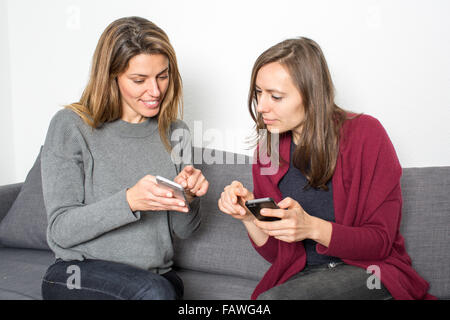 Le ragazze che mostra pettegolezzi sullo smartphone mentre è seduto in salotto Foto Stock