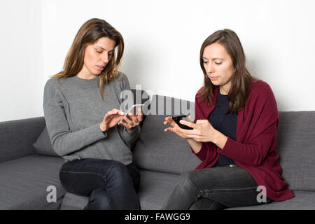 Le ragazze che mostra pettegolezzi sullo smartphone mentre è seduto in salotto Foto Stock