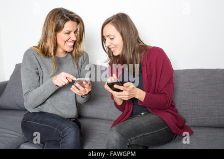 Le ragazze che mostra pettegolezzi sullo smartphone mentre è seduto in salotto Foto Stock