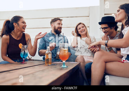 Ritratto di felice giovani seduti insieme e ridere. Multirazziale godendo di amici a una festa con cocktail sul tavolo. Foto Stock