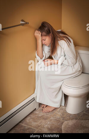 Ragazza adolescente seduto in bagno sul sedile di gabinetto cercando infelice Foto Stock