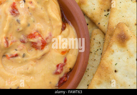 Top vista ravvicinata di una piccola ciotola con un serving di hummus con peperoni rossi plus pita snack crackers. Foto Stock