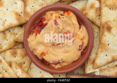 Una piccola ciotola con un serving di hummus con peperoni rossi plus pita snack crackers. Foto Stock