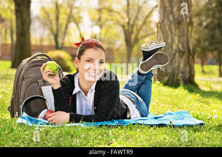 Vita sana con la natura intorno a noi. Bella sorridente ragazza giovane sdraiati sull'erba nel parco tenendo un apple, prendendo una pausa dallo studio. Foto Stock