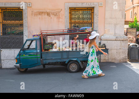 Uomo che guarda donna, vista di due uomini che guardano una giovane donna elegante in un lungo vestito estivo mentre passa un camion di venditori di frutta a Taormina, Sicilia. Foto Stock