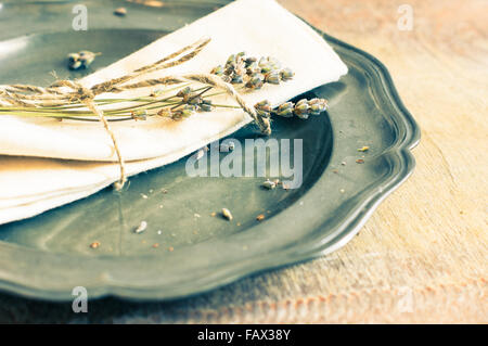 Tavolo rustico con impostazione argenteria vintage e la piastra con secchi fiori di lavanda. Immagine dai toni Foto Stock