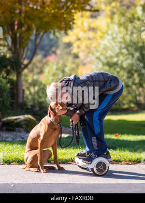 REDDING, CA, Stati Uniti d'America - 24 novembre 2015: ragazzo adolescente passeggiate cane con auto-bilanciare due-scooter a ruote, chiamato anche un hoverboard. Foto Stock