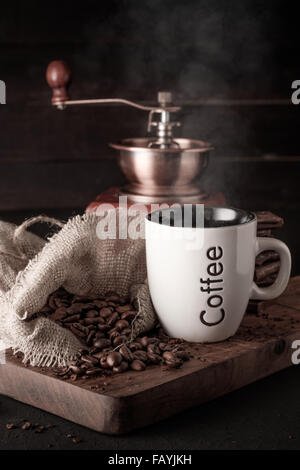 Tazza di caffè e un sacchetto di chicchi di caffè su sfondo di legno. Tazza di caffè caldo con il cioccolato. Foto Stock