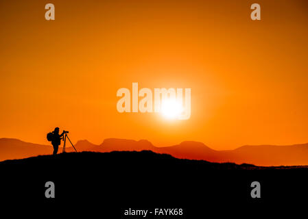 Tramonto e fotografo con un treppiede, Flatey Isola, Breidafjordur, Occidentale, Islanda Foto Stock