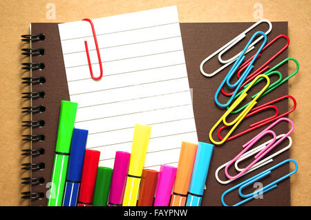 Nota graffetta su notebook con colorati pennarello e graffette sul marrone sfondo di cartone Foto Stock