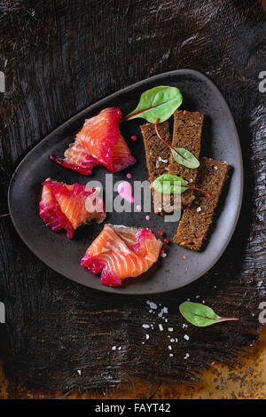 Triangolare piastra in ceramica con fette di filetto di salmone, salate con succo di barbabietola, servita con frumento integrale toast, foglie di insalata e Foto Stock