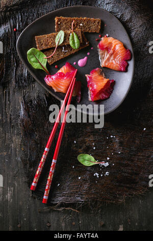 Triangolare piastra in ceramica con fette di filetto di salmone, salate con succo di barbabietola, servita con frumento integrale toast, foglie di insalata e Foto Stock