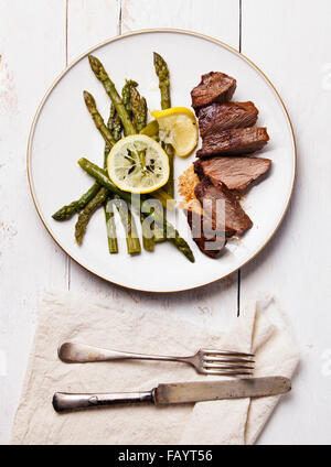 Arrosto di manzo con gli asparagi sulla piastra bianca su sfondo di legno Foto Stock