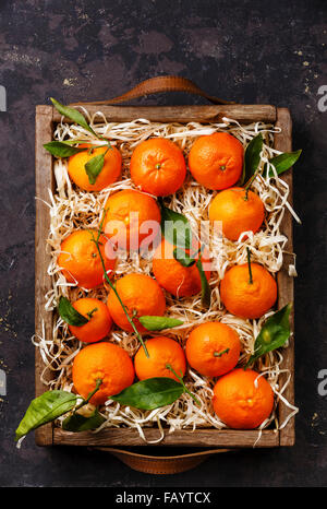 Tangerini con foglie in una scatola di legno su sfondo nero Foto Stock