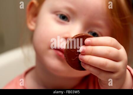 Una bambina di tre anni in possesso di una moneta di cioccolato Foto Stock