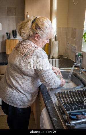 Lavorato a maglia,una signora anziana in cucina lavaggio fino Foto Stock