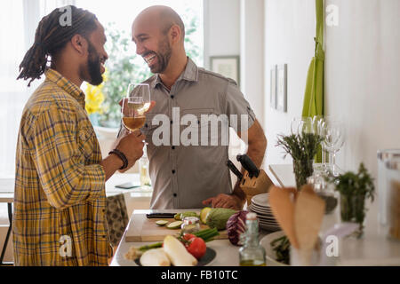 Smiley coppia omosessuale di bere vino in cucina Foto Stock