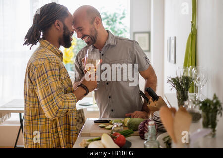 Smiley coppia omosessuale di bere vino in cucina Foto Stock