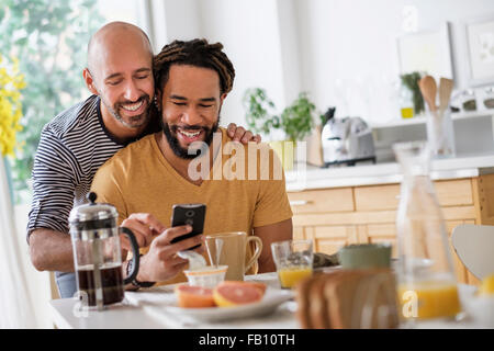 Smiley coppia omosessuale utilizzando smart phone al tavolo per la cena Foto Stock