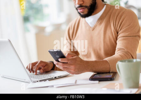 Uomo al lavoro con il computer portatile a tavola e tenendo premuto smart phone Foto Stock