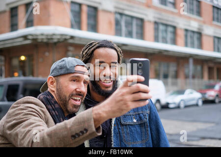 Smiley coppia omosessuale tenendo selfie con smart phone in strada Foto Stock