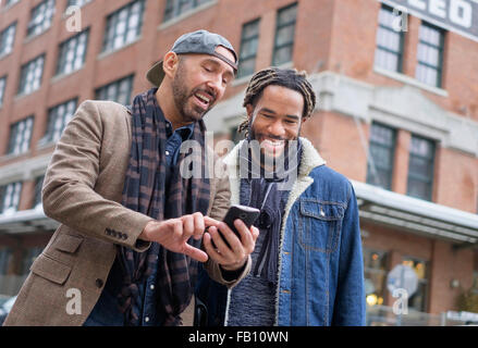 Smiley coppia omosessuale guardando smart phone in strada Foto Stock
