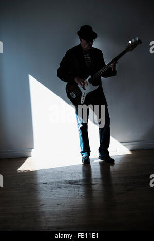 Uomo a suonare il basso chitarra in stanza vuota Foto Stock