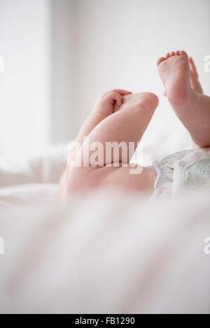 Baby girl (12-17 mesi) disteso con le mani sui piedi Foto Stock