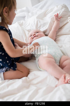 Baby girl (12-17 mesi) con la sorella (2-3) sul letto Foto Stock