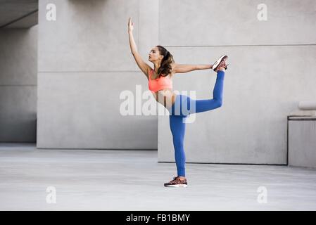 Vista laterale della giovane donna in equilibrio su una gamba, gamba sollevata tenendo la caviglia stretching Foto Stock