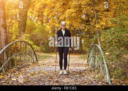 Femmina Senior Nordic Walker attraversando il ponte pedonale in autunno park Foto Stock
