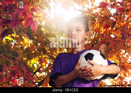 Le ragazze di tree coperto di foglie di autunno tenendo il calcio alla ricerca di distanza Foto Stock