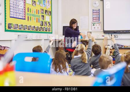 Insegnante interrogando i bambini seduti sul pavimento nella scuola elementare classroom Foto Stock