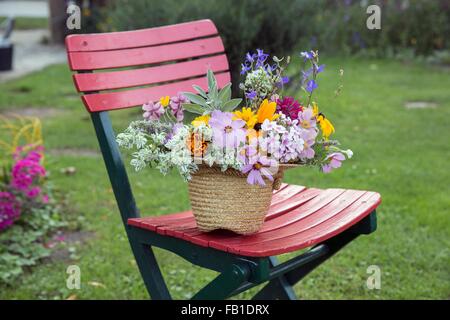 Fiori recisi freschi nel cappello di paglia, sulla sedia da giardino Foto Stock