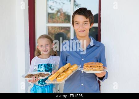 Ritratto di ragazzo adolescente e la sorella il trasporto di torte sul patio Foto Stock