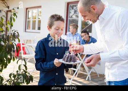 Metà uomo adulto figli di illuminazione torta di compleanno candele sul patio Foto Stock