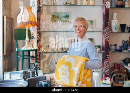 Ritratto di donna matura pieghevole coperta di giallo nel negozio vintage Foto Stock