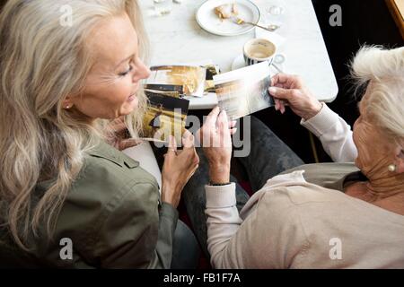 Madre e figlia insieme seduta in cafe, guardando le fotografie, vista posteriore Foto Stock