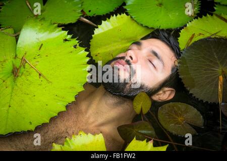 Angolo di Alta Vista del barbuto giovane floating tra ninfee, gli occhi chiusi, Taiba, Ceara, Brasile Foto Stock