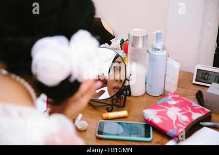 Al di sopra della spalla vista della giovane donna alla toeletta applicando specchio dello specchio Foto Stock