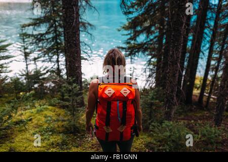 Vista posteriore metà donna adulta che trasportano il colore arancione zaino acqua foresta Moraine Lake il Parco Nazionale di Banff Alberta Canada Foto Stock