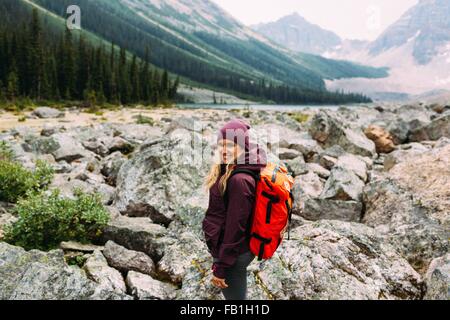 Vista laterale metà donna adulta paesaggio roccioso che porta uno zaino fotocamera a sorridere al Lago Moraine il Parco Nazionale di Banff Alberta Canada Foto Stock