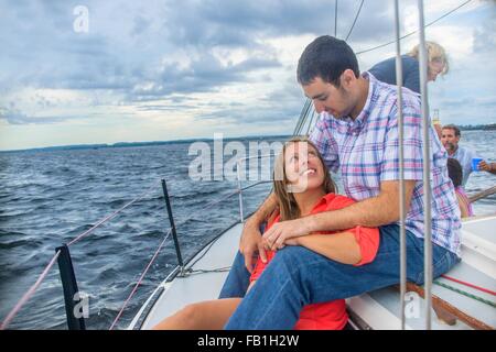 Giovane donna seduta tra giovani mans gambe su barche a vela, faccia a faccia sorridente Foto Stock