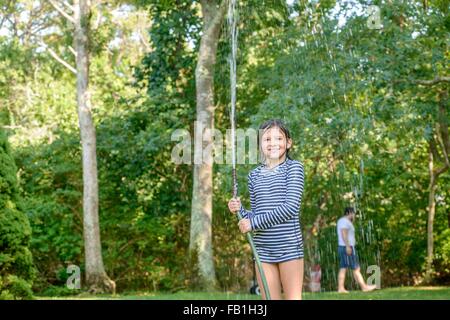 Giovane ragazza in giardino, tenendo il tubo flessibile da giardino Foto Stock