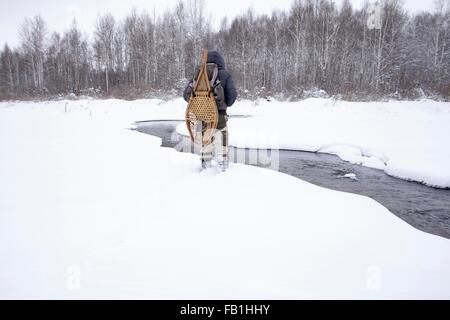 Vista posteriore della metà uomo adulto nella neve campo coperto dal fiume con le racchette da neve tradizionali, Ural, Russia Foto Stock