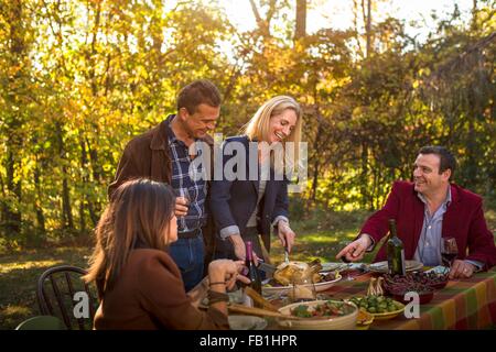 Due coppie mature che serve cena arrosto al party in giardino Foto Stock