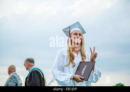 Giovani laureati femmina facendo segno di pace alla cerimonia di consegna dei diplomi Foto Stock