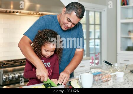 Padre aiutando la figlia tritare verdure in cucina Foto Stock